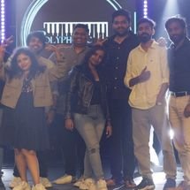 Band members performing on stage under dramatic lighting with purple and blue spotlights, energetic concert atmosphere, audience not visible